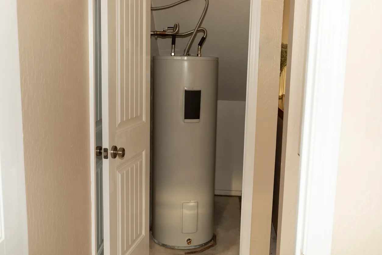 A traditional, cylindrical water heater is visible through an open closet door, showing its placement in a small, utility space.