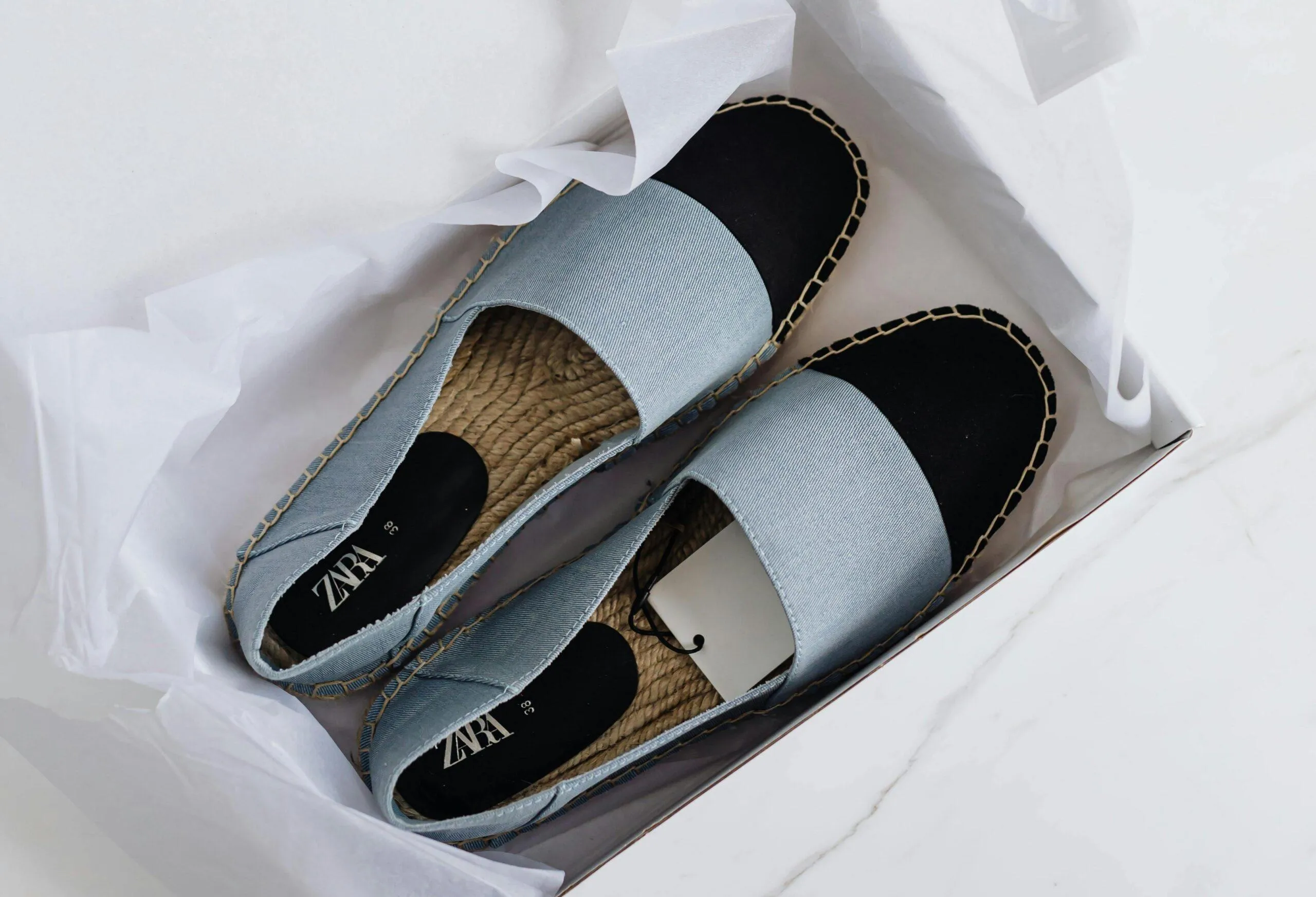 A pair of blue espadrilles with the shopping tag in a white box.