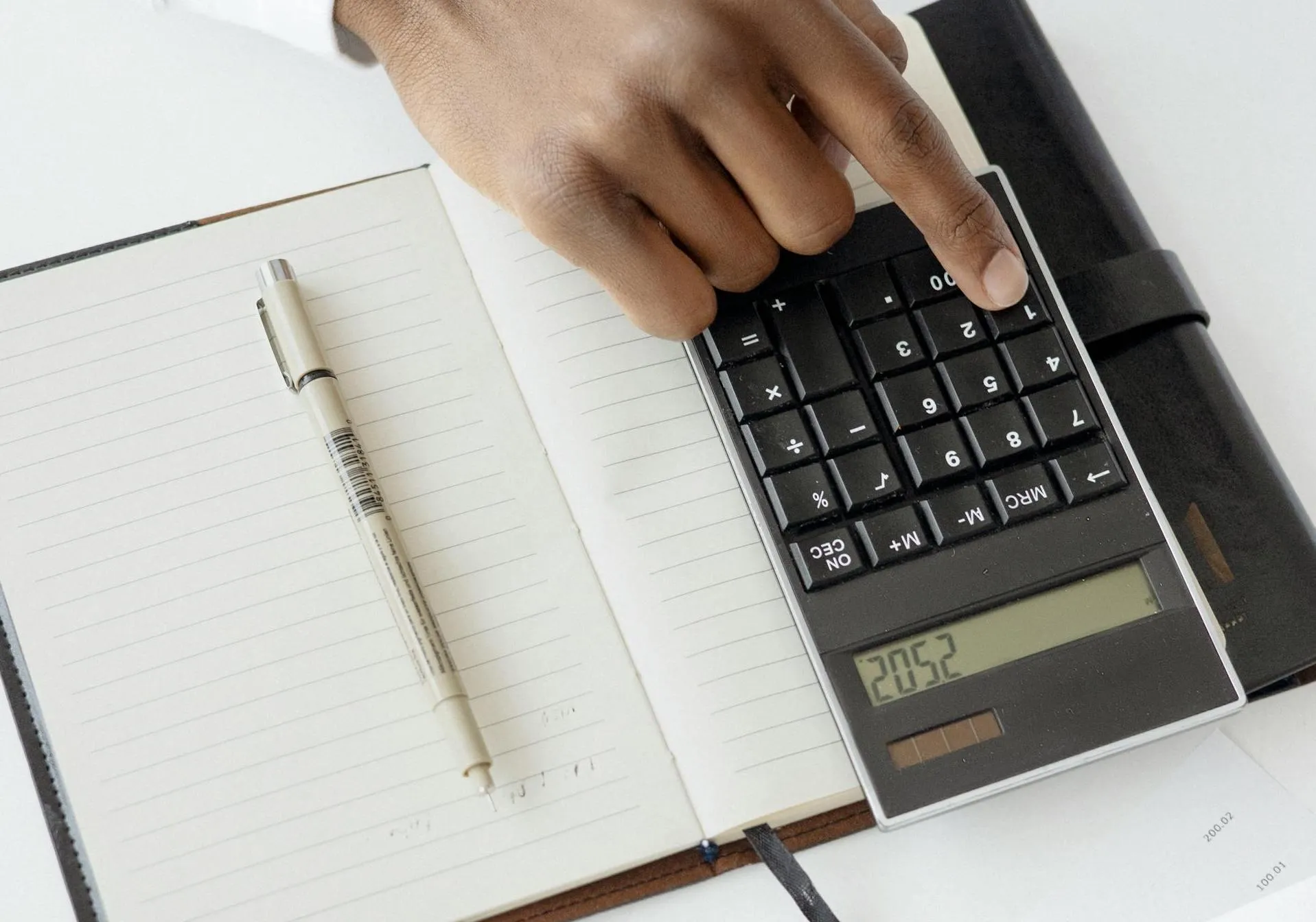 A hand reaches for a calculator sitting on top of a notepad.