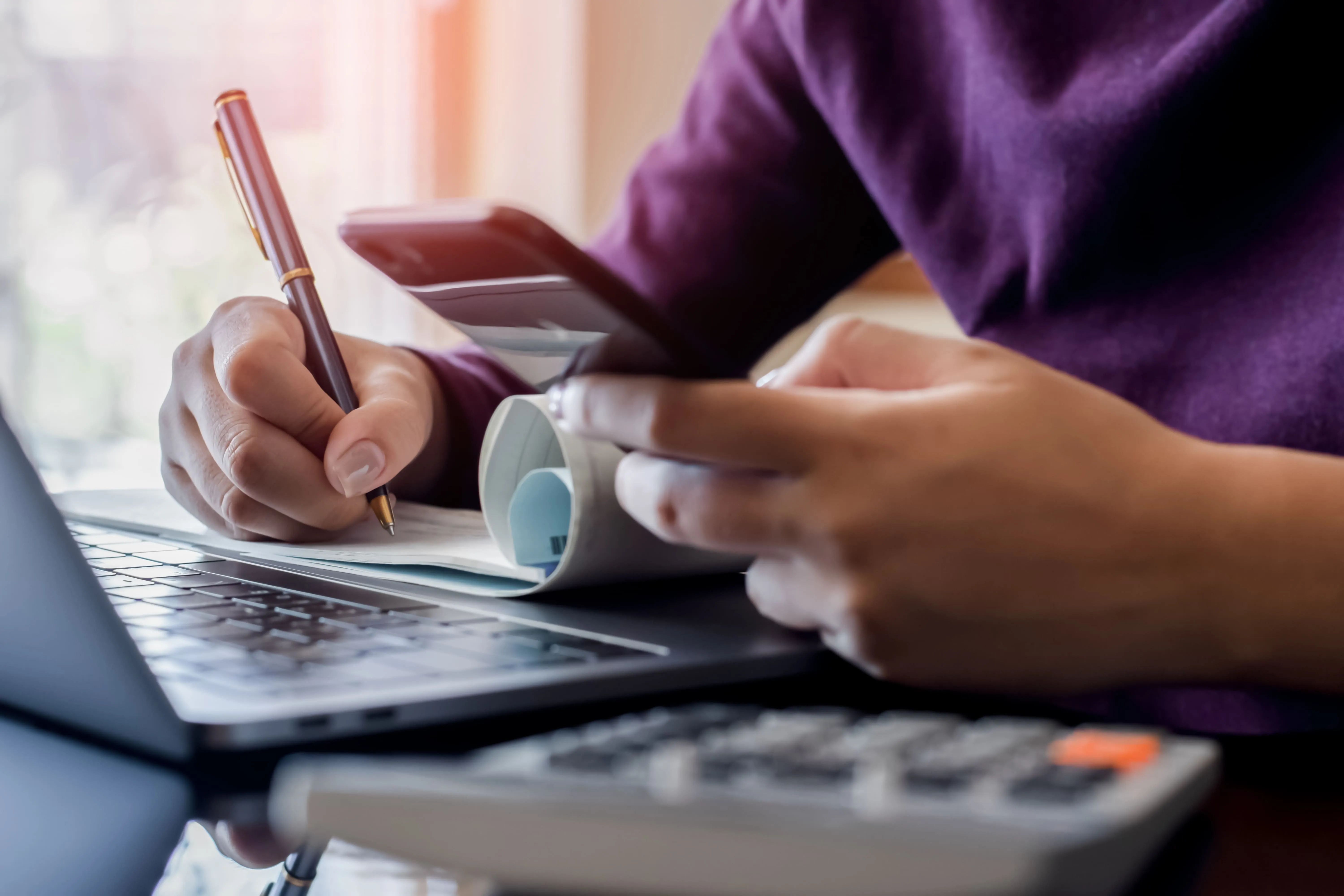 A woman with a notebook and digital devices, evaluating the best sales tax automation software for SaaS