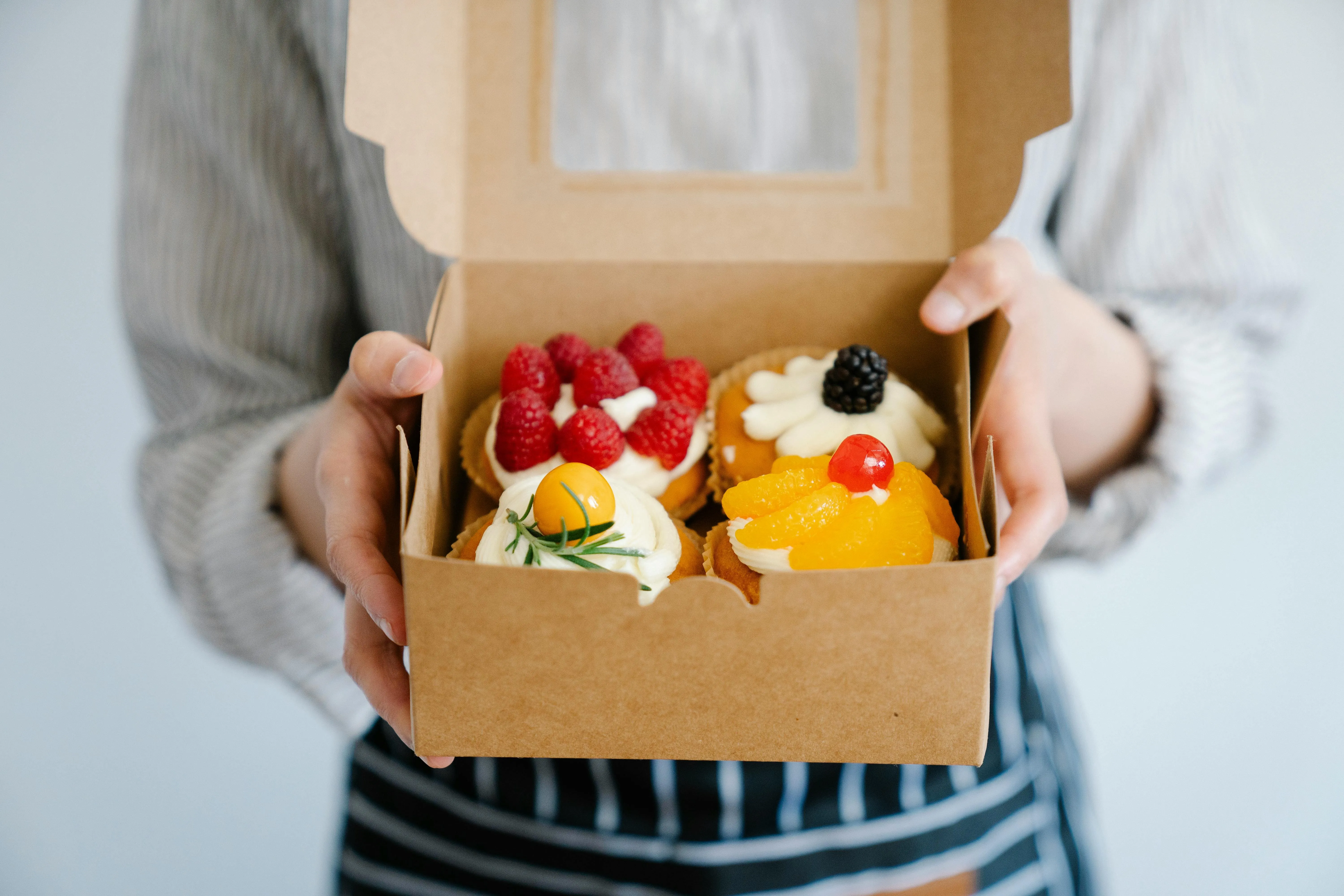 Baker holding a box of cupcakes with fresh fruit toppings