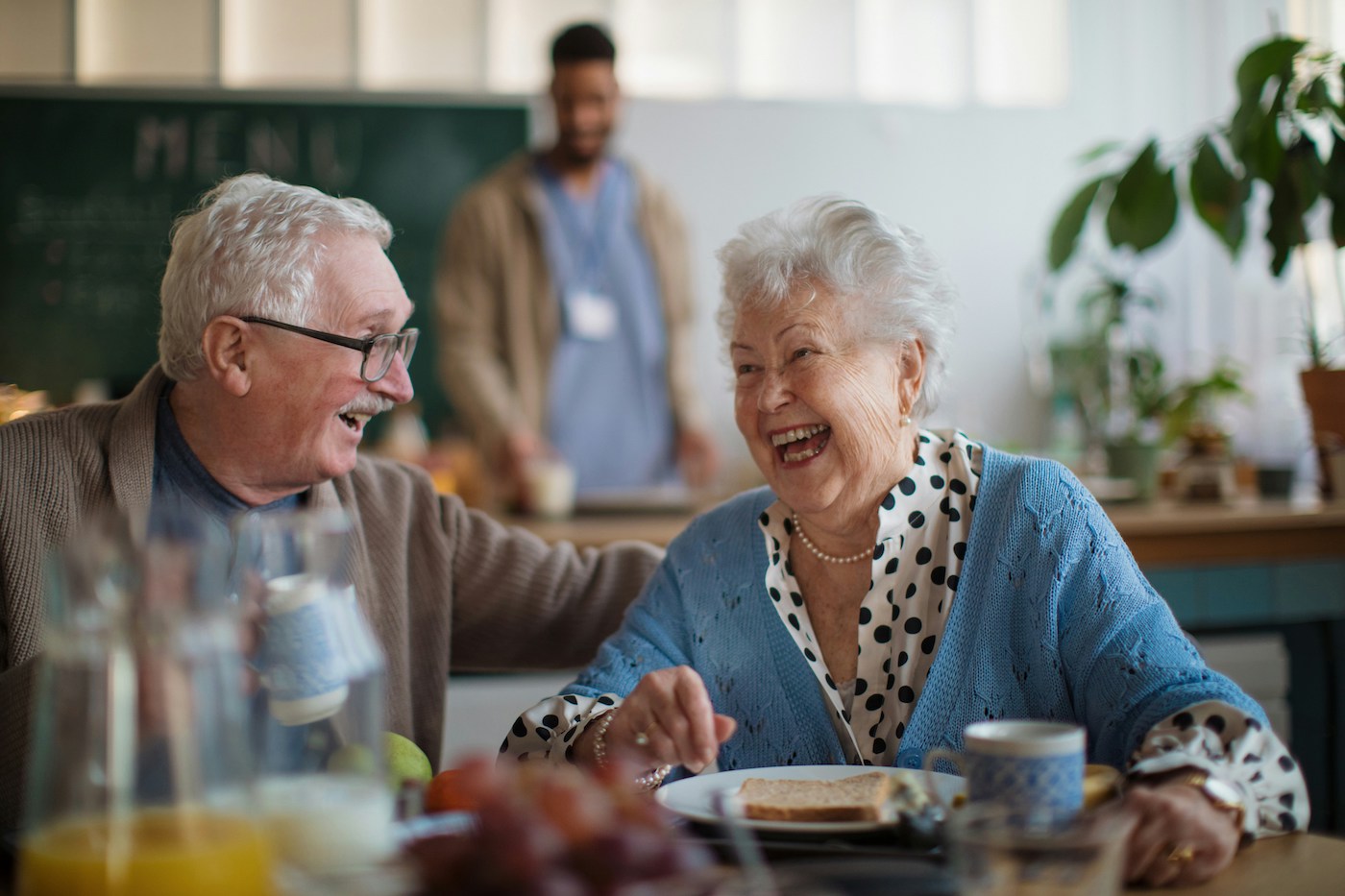 couple laughing having lunch while nurse prepares food