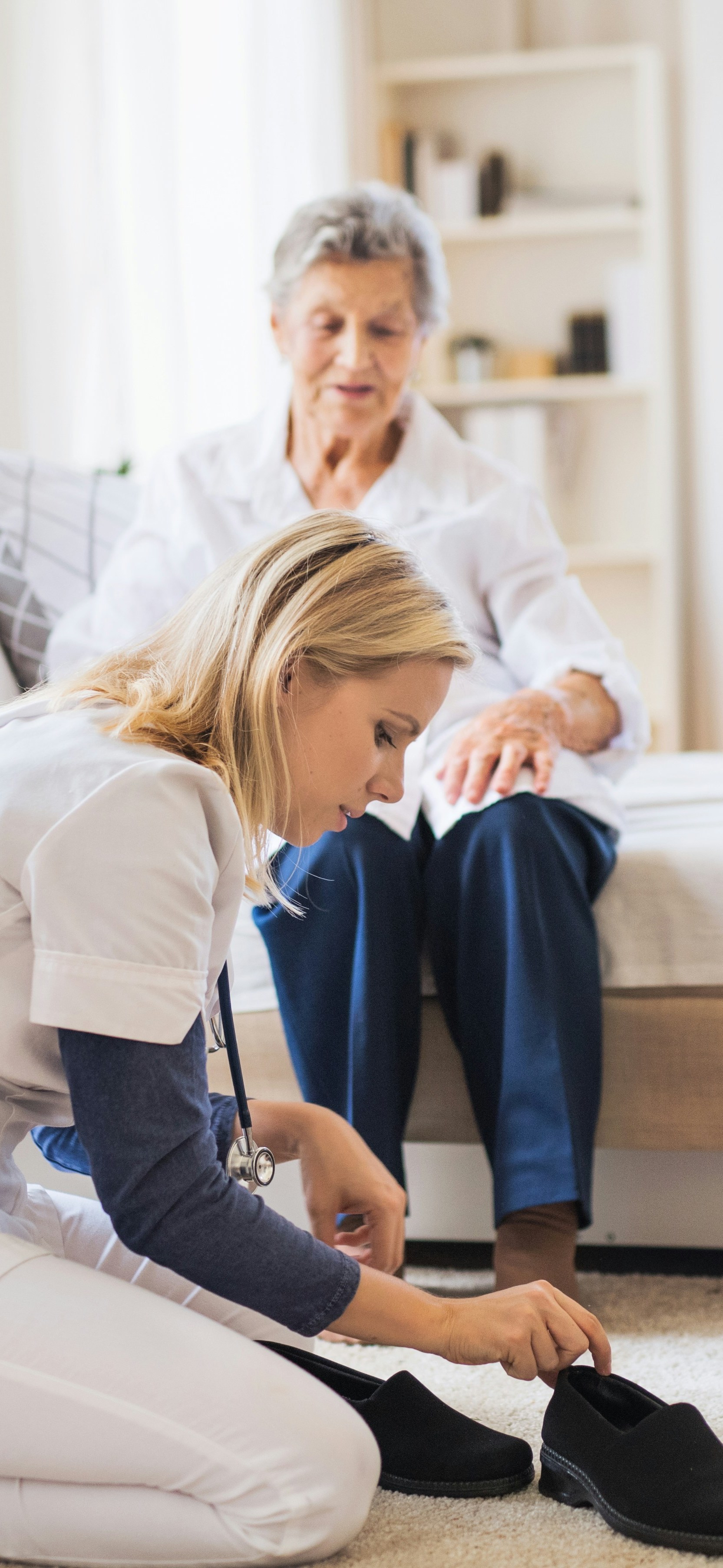 nurse helping elderly women put her shoes on in a nursing home