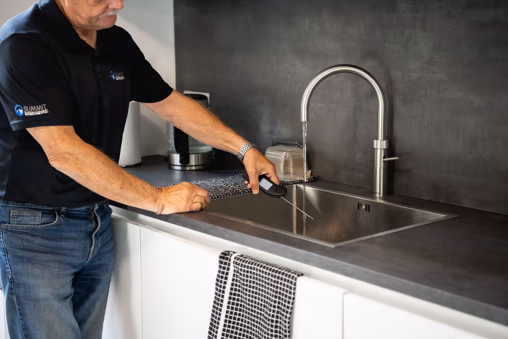 Man pouring liquid from a bottle into a kitchen sink with a modern faucet.