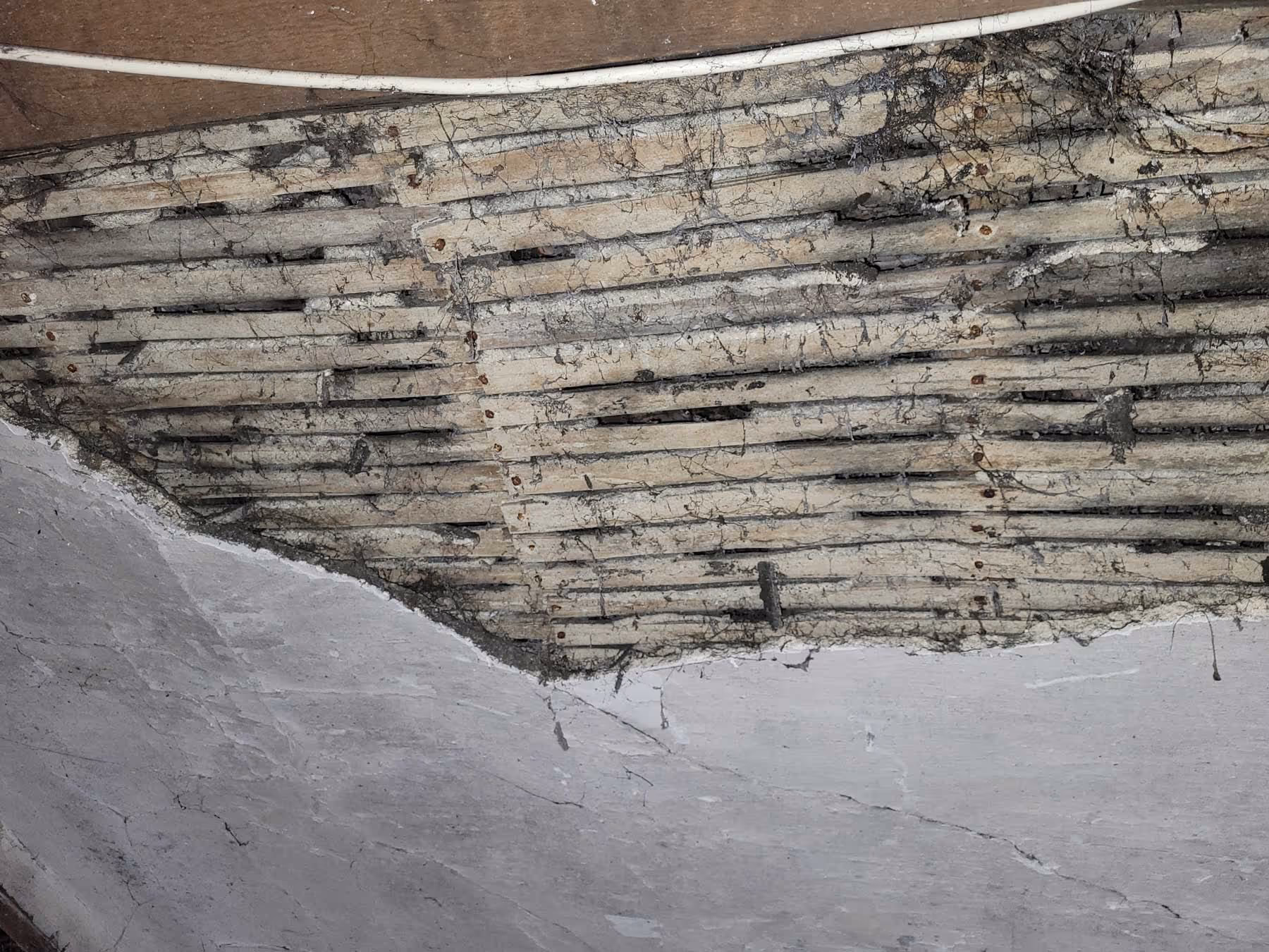 Exposed wooden lath beneath a damaged plaster ceiling, showing signs of age and wear.