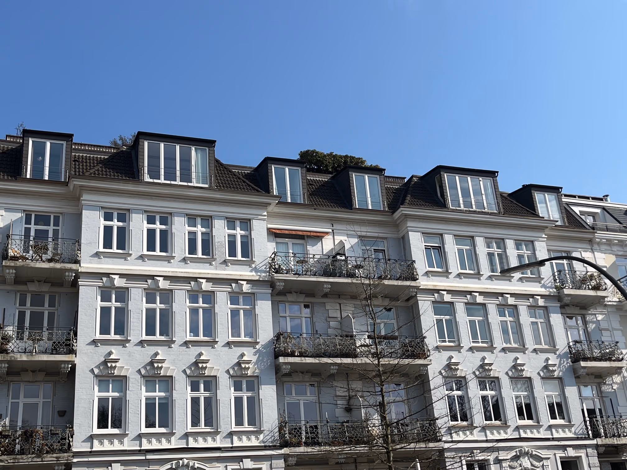 Weiße Altbauwohnungen mit Balkonen und Gauben unter klarem blauem Himmel.