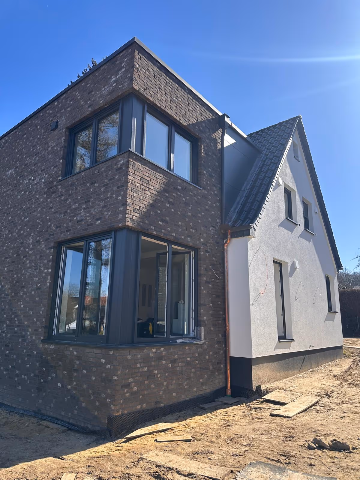 Modernes zweistöckiges Haus mit brauner Klinkerfassade und weißem Putz unter klarem blauem Himmel.