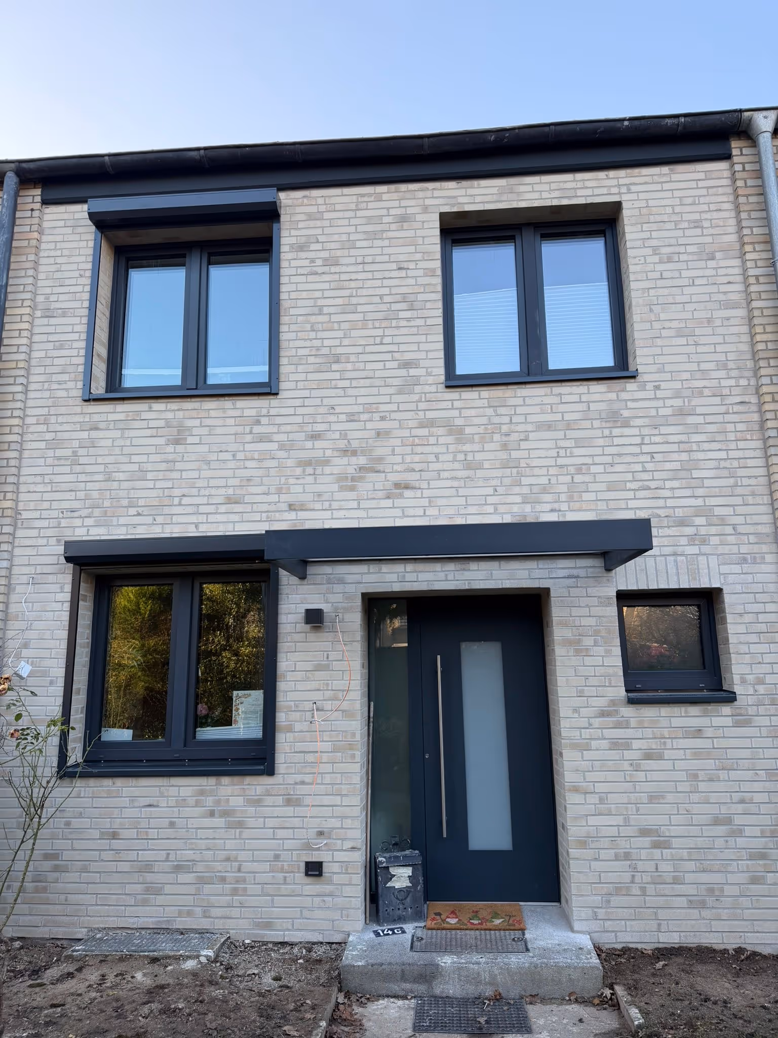 Eingang eines Hauses mit hellem Klinker, dunkelblauer Tür und vier Fenstern, davor eine kleine Treppe.