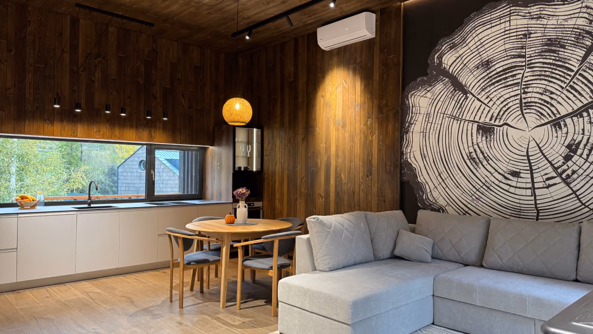 Modern living room with gray sectional sofa, wood dining table, large window, and a tree ring wall art.