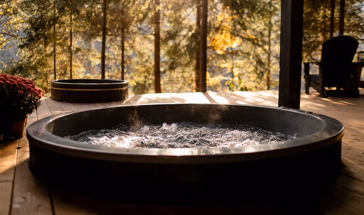 Two bubbling outdoor hot tubs on a wooden deck surrounded by trees in warm sunlight.