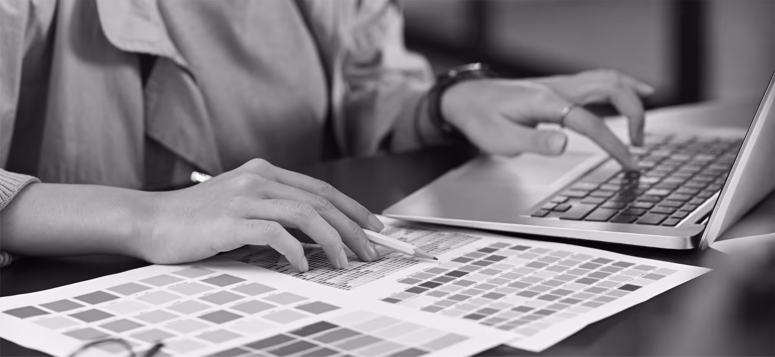 Person working with color swatches and using a laptop keyboard at a desk.