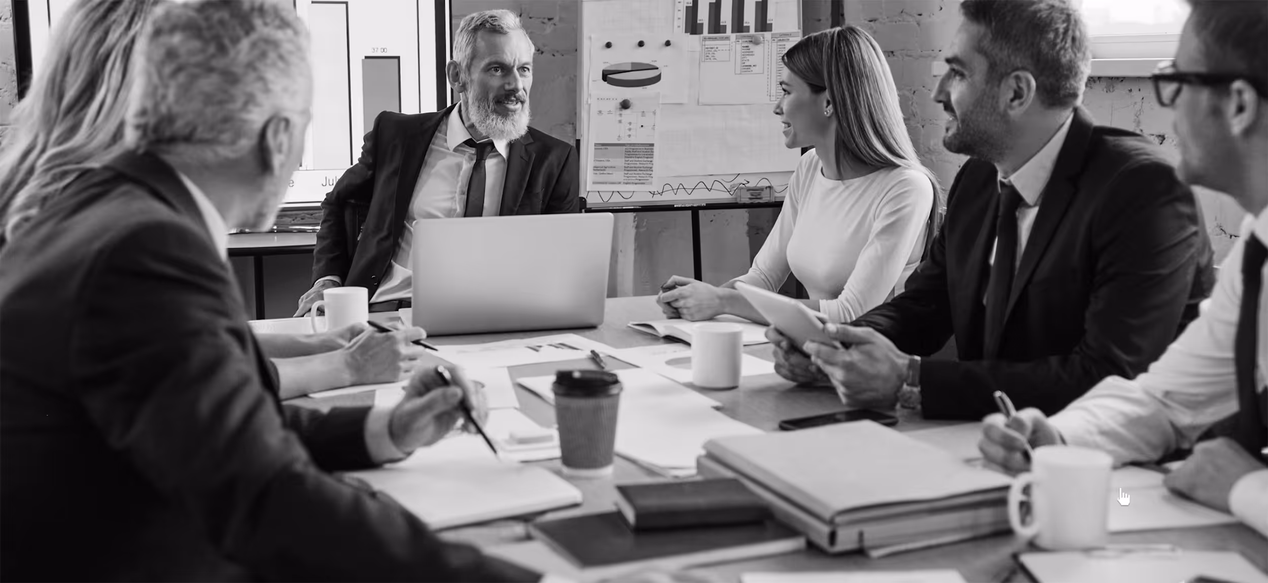 Business team in a meeting room engaged in discussion with charts and laptop on the table.