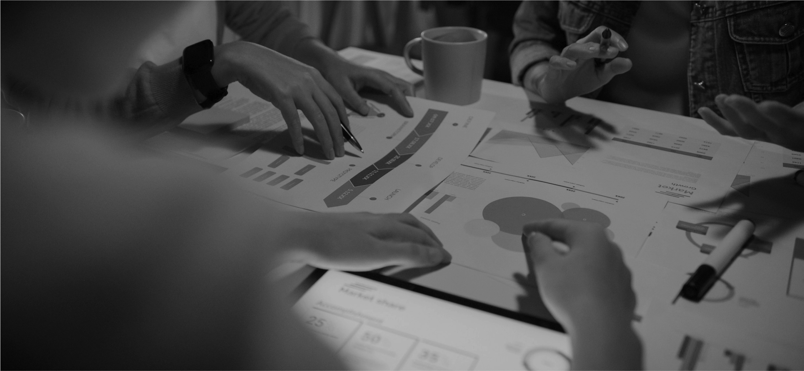 People discussing marketing charts and data sheets on a table, with pens and a coffee mug nearby.