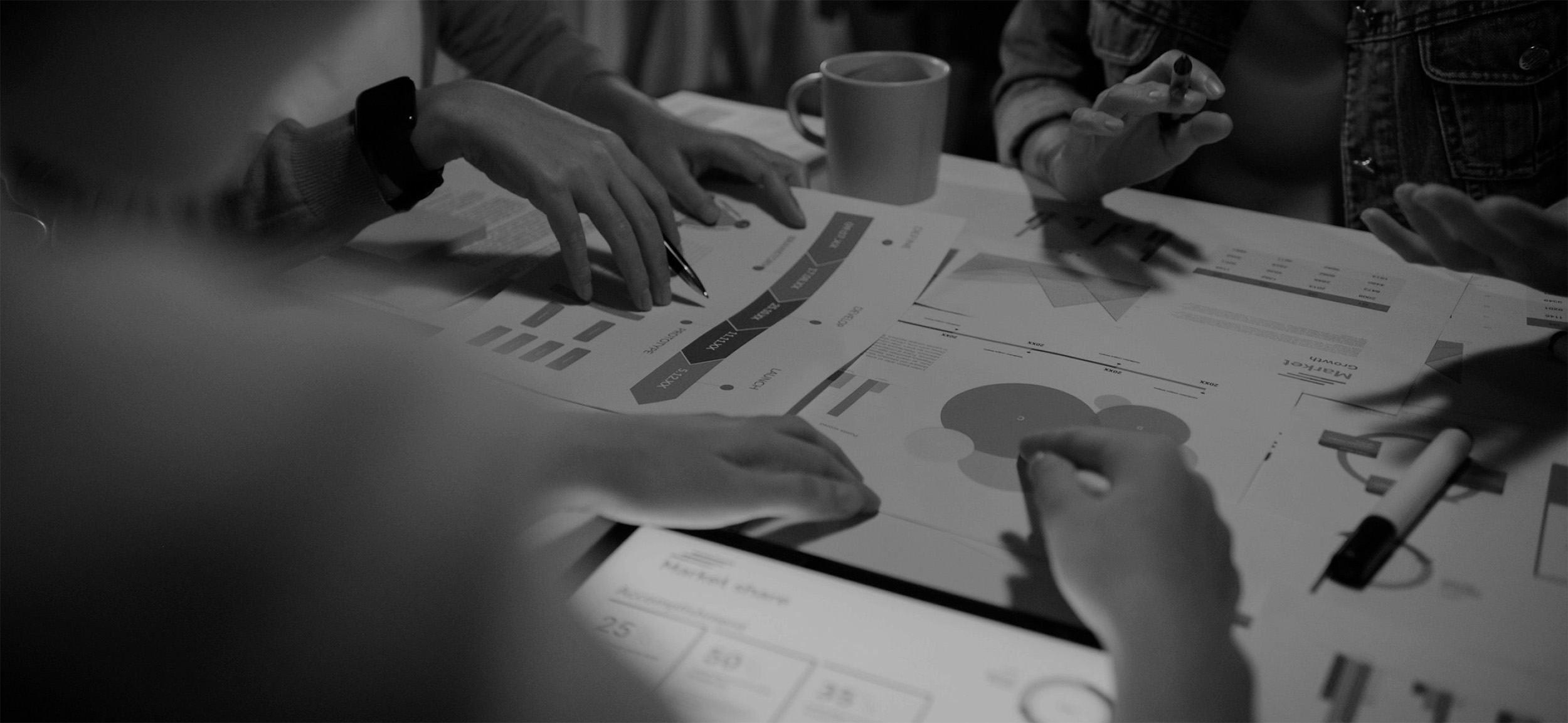 People collaborating at a table with documents displaying charts and graphs, and a coffee cup nearby.