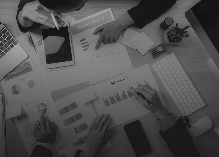Overhead view of multiple people analyzing business and sales reports with charts, using a tablet and laptop on a desk.
