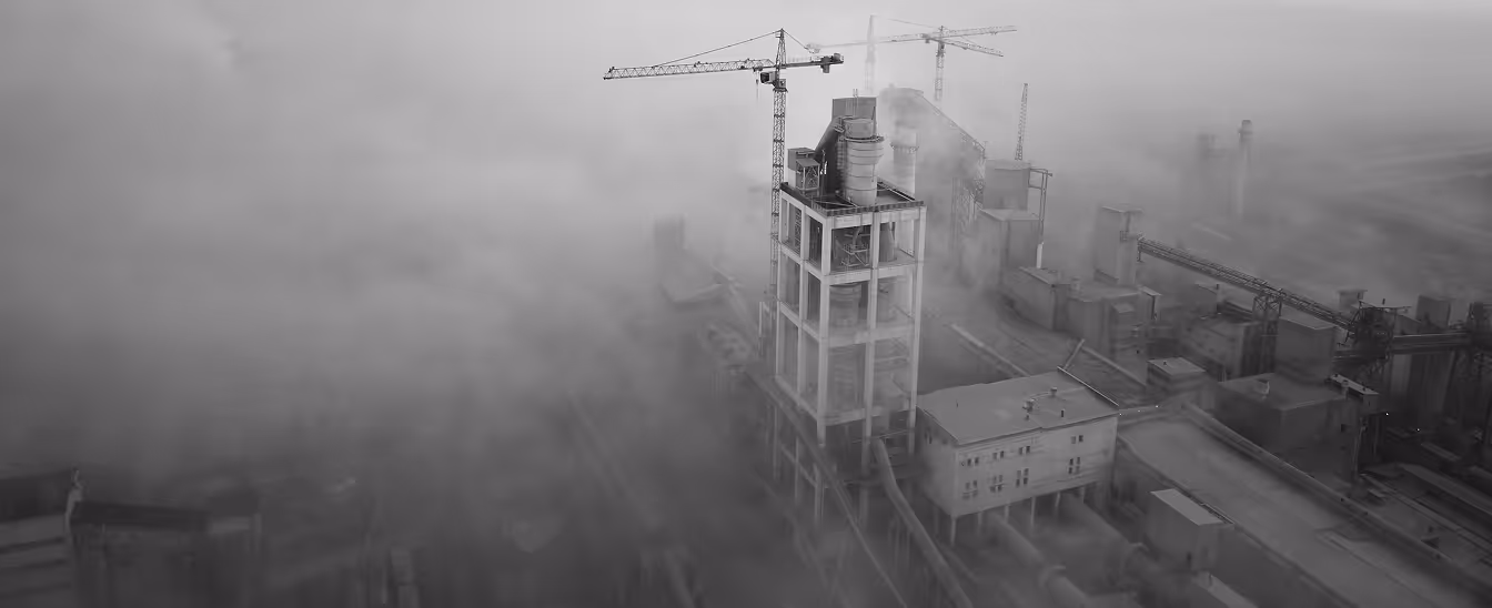 Industrial facility or factory partially obscured by thick smoke or fog with cranes and large structures visible.