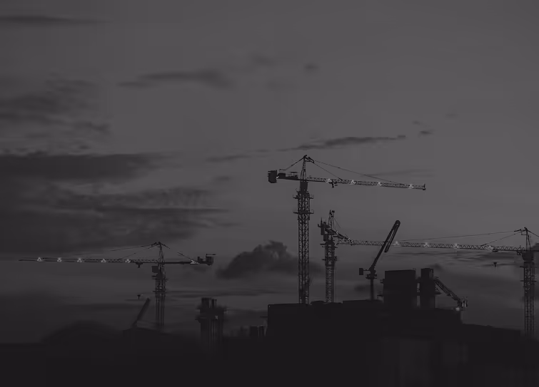 Silhouette of multiple tower cranes at a construction site against a cloudy evening sky.