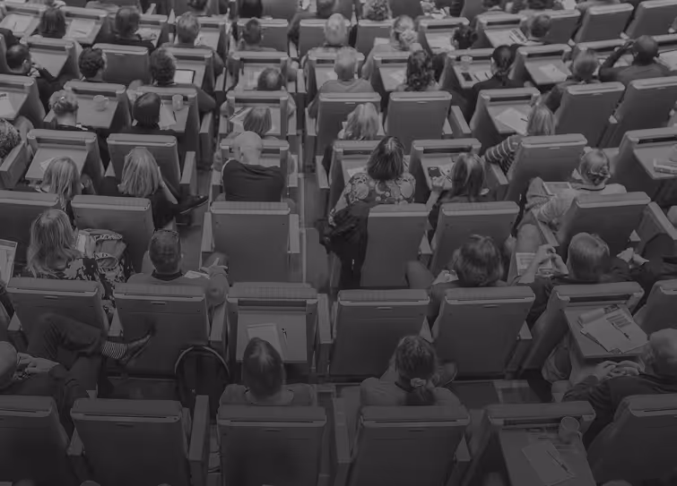 Overhead view of an audience seated in rows of chairs, facing forward in a lecture or conference setting.