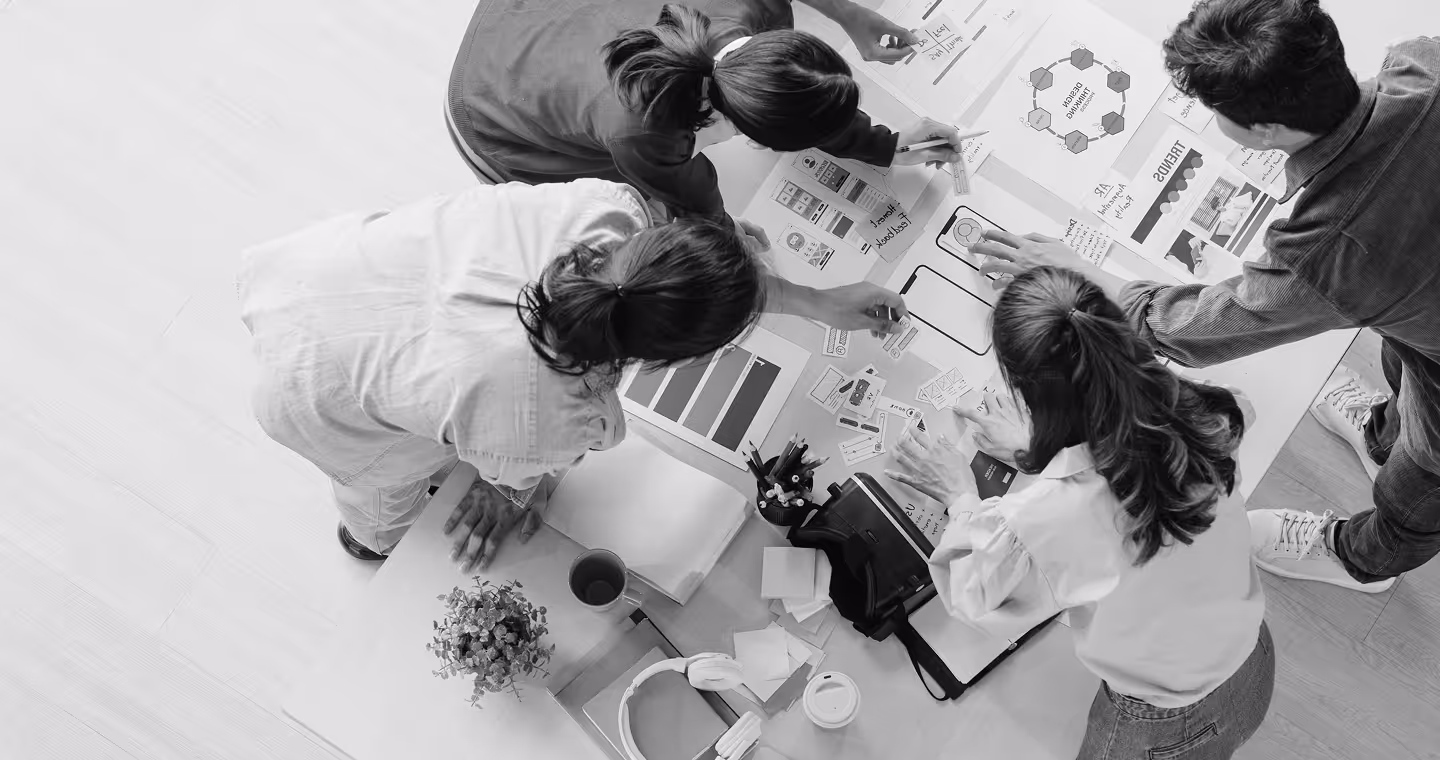 Top view of a group of four people collaborating over design sketches and charts spread on a table.