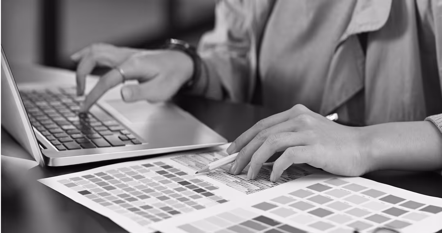 Person working on a laptop and selecting colors on printed color swatch sheets with a pencil.