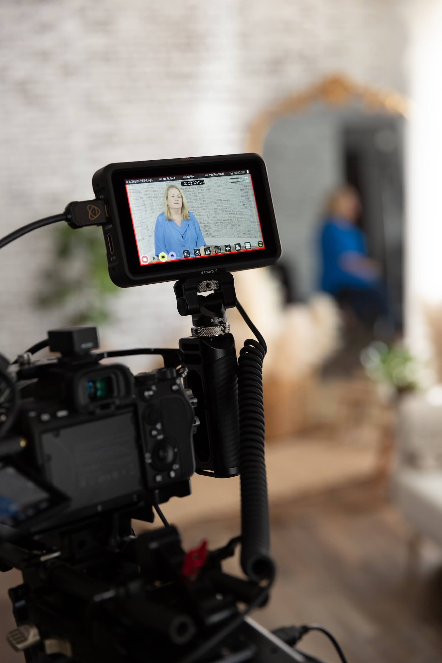 Person with curly hair and glasses editing video on a desktop computer in a cozy workspace.