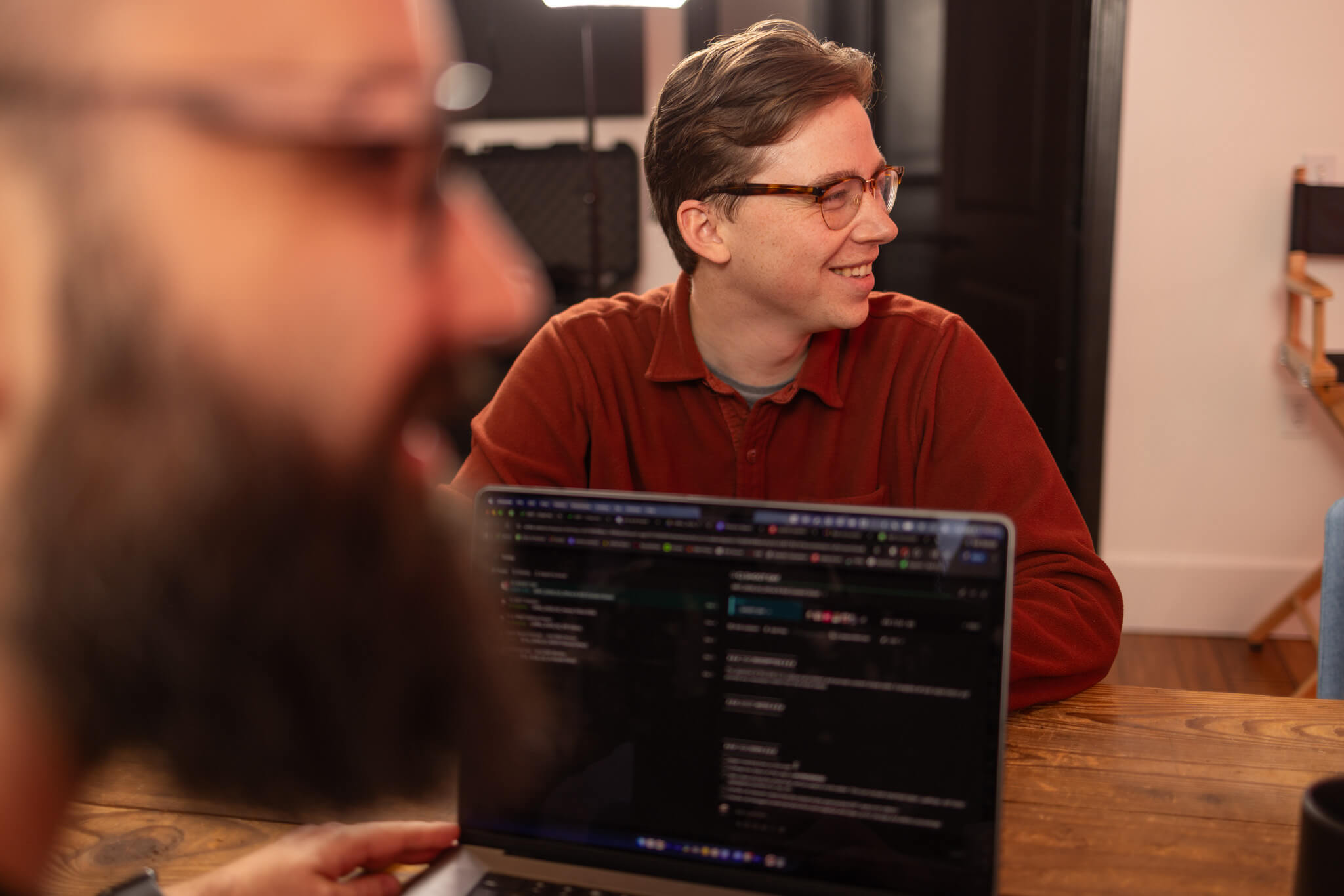Black and white photo of a busy city street with pedestrians crossing a wide zebra crosswalk surrounded by tall buildings and illuminated billboards at sunset.