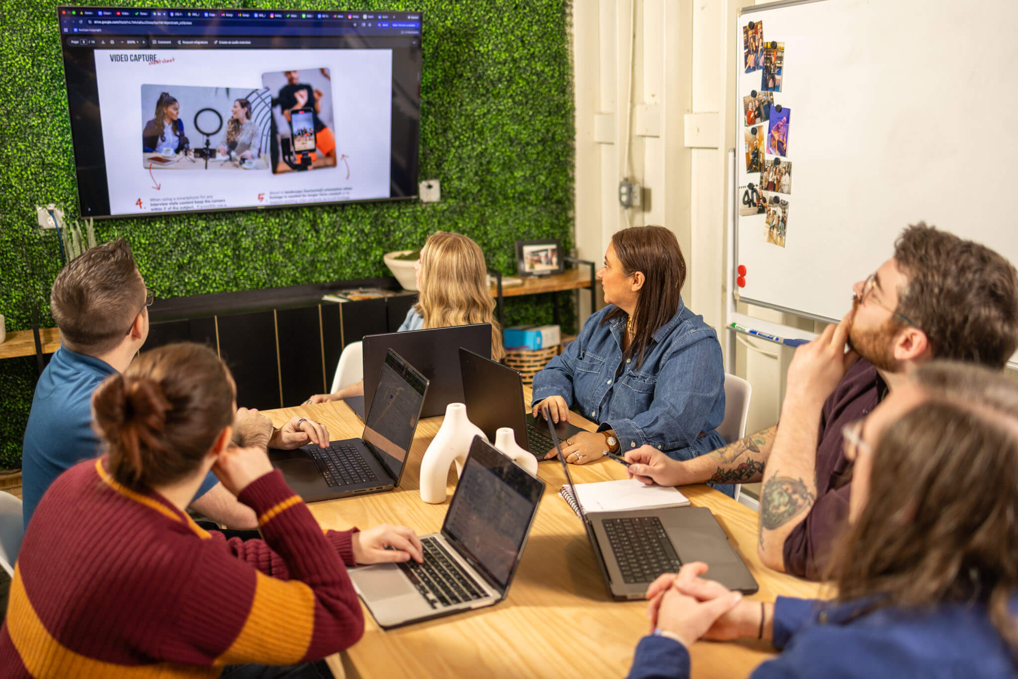 Two colleagues collaborating at a table covered with fabric samples and design papers in a modern office with large windows.