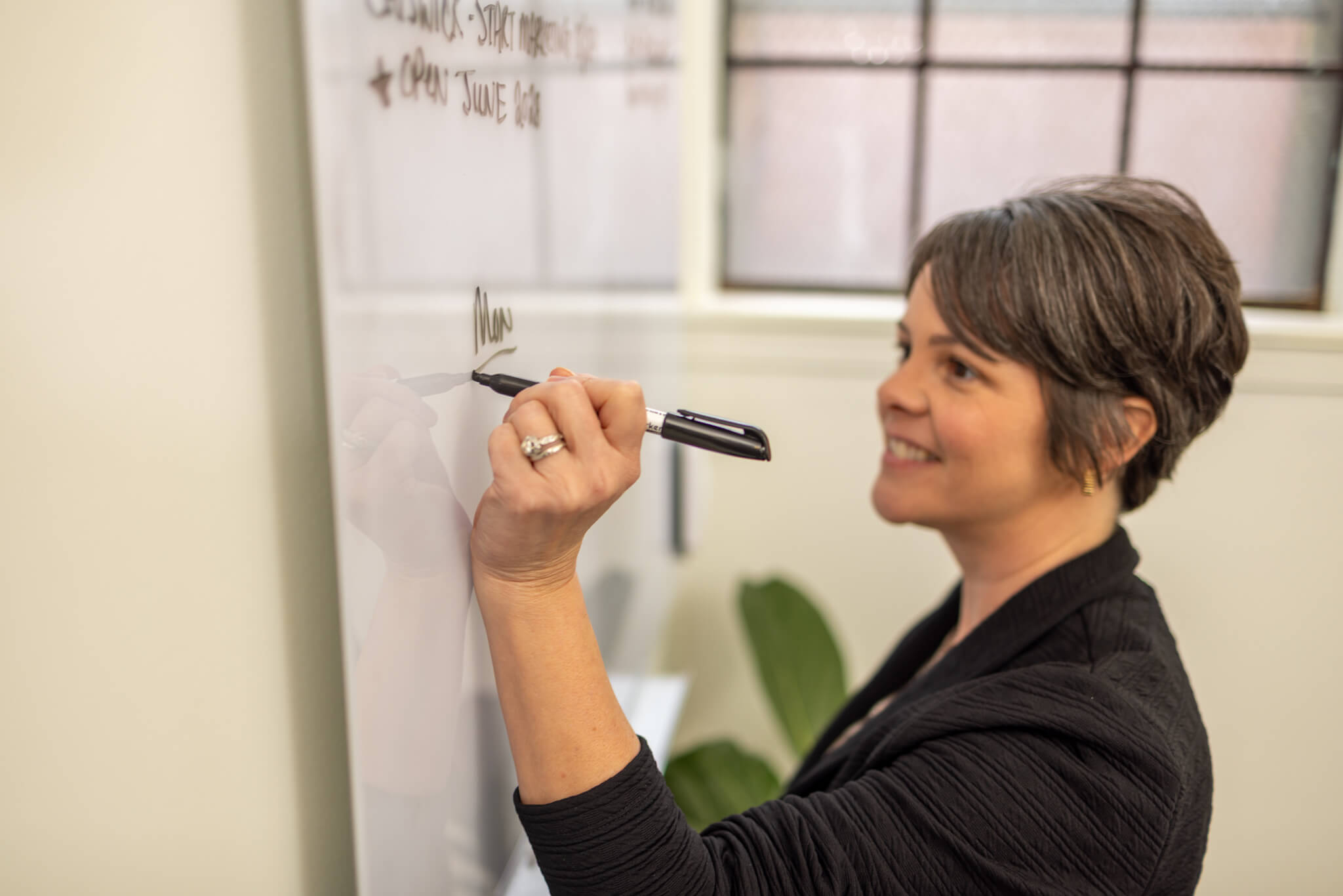 Two people sitting at a table covered with fabric samples and design papers, looking at a laptop together in a modern office with large windows.