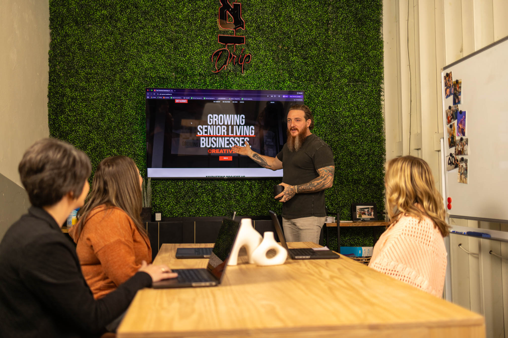 Group of seven people sitting around a wooden table in a modern kitchen, engaged in conversation with drinks and snacks on the table.
