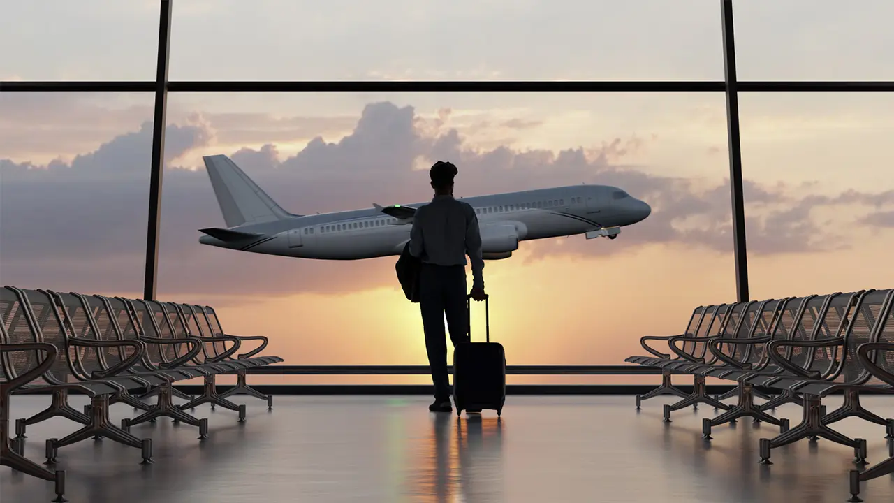 A silhouetted traveler standing in an airport terminal with a rolling suitcase watching a plane take off at sunset, representing the risk of travel identity theft affecting airline and cruise passengers in 2026.