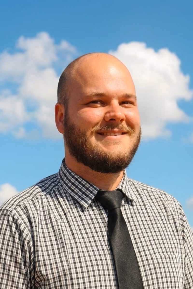 Dan Esterhuizen smiling in a checked shirt and tie against blue sky