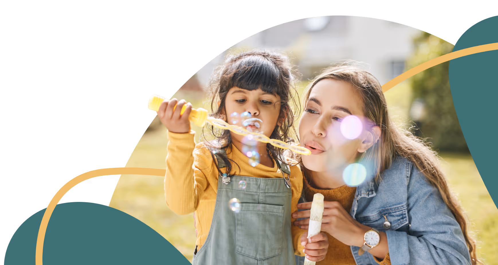 Woman and young girl outdoors blowing soap bubbles together on a sunny day.