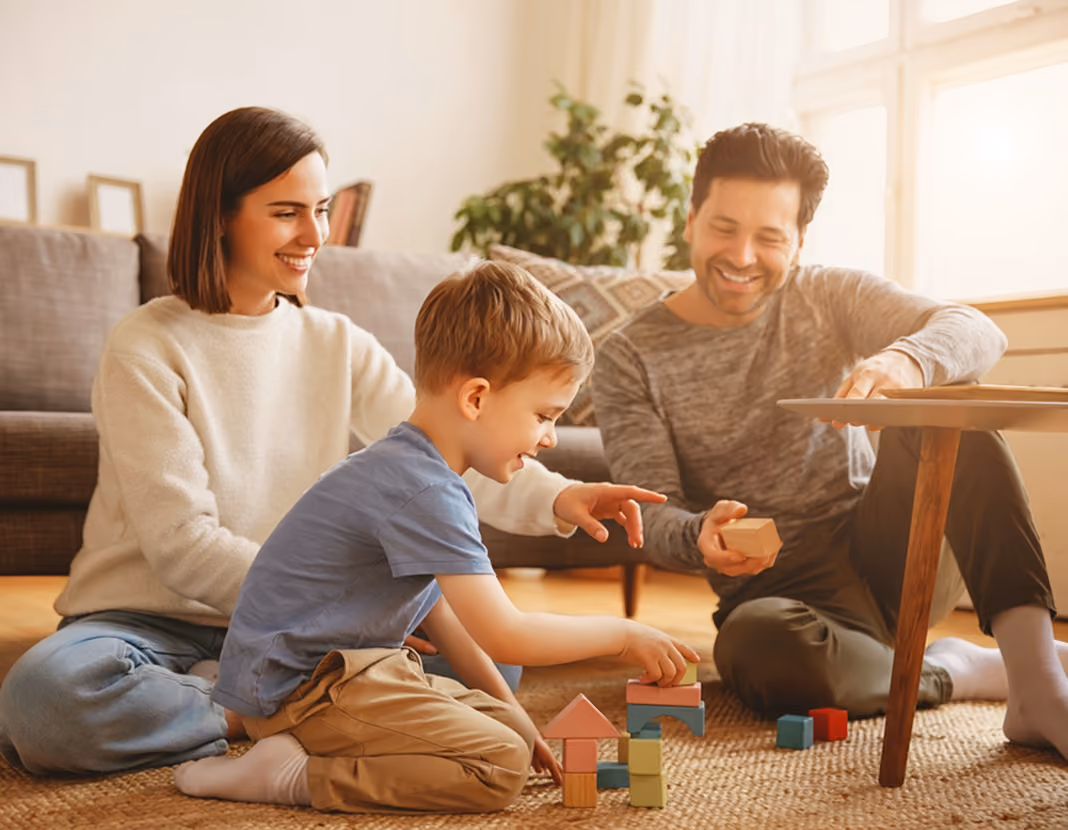 Parents and child sitting on the floor in living room playing and stacking wooden blocks together.