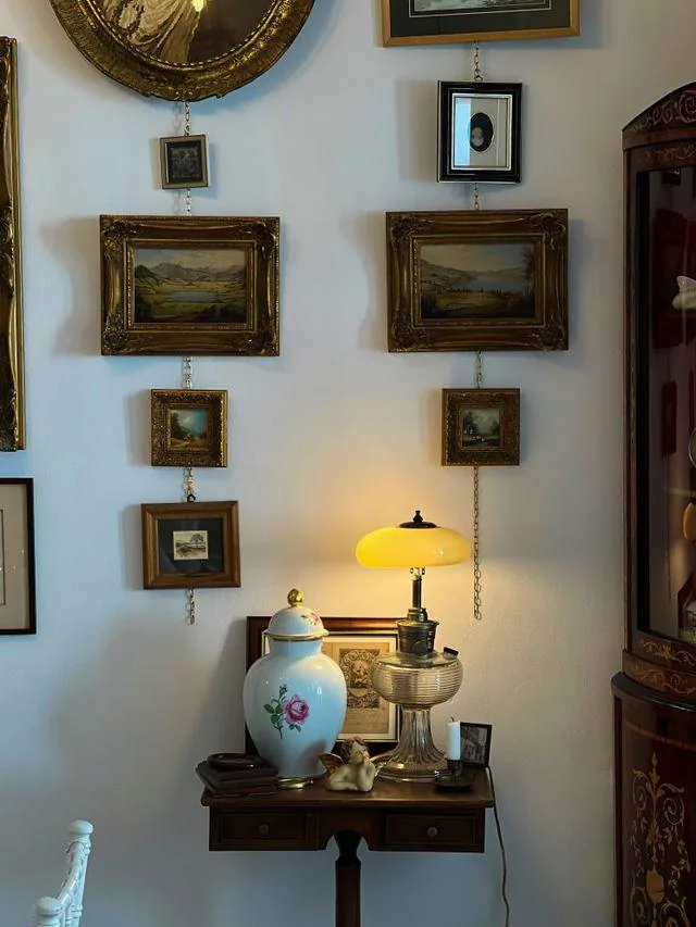Gallery wall of framed landscape paintings above a small table with a glowing yellow lamp