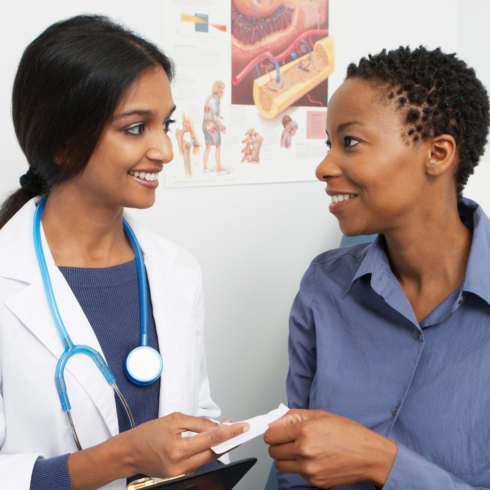 Female doctor with stethoscope handing a prescription to a smiling patient in a medical office.