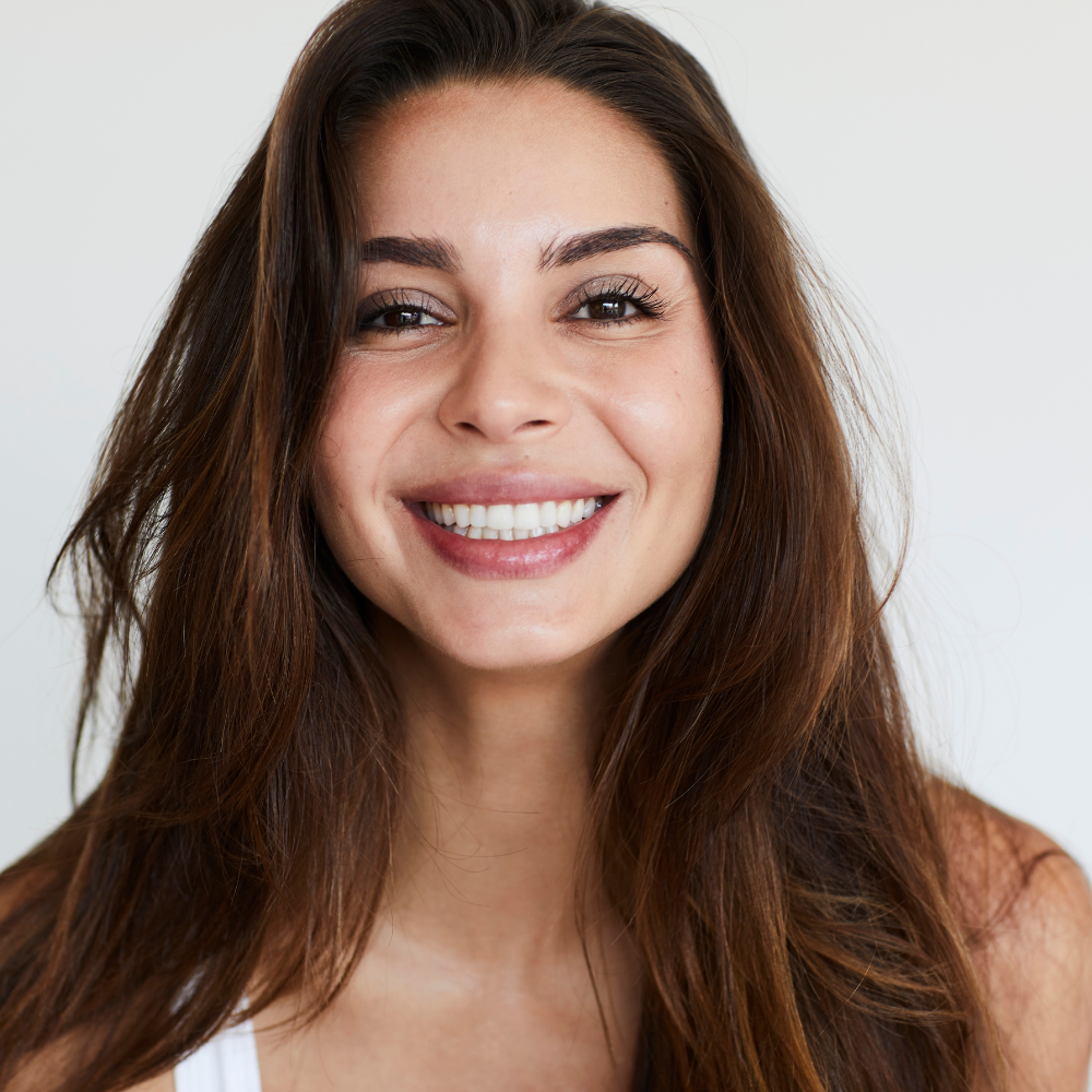 Smiling woman with long brown hair and clear skin against a neutral background.