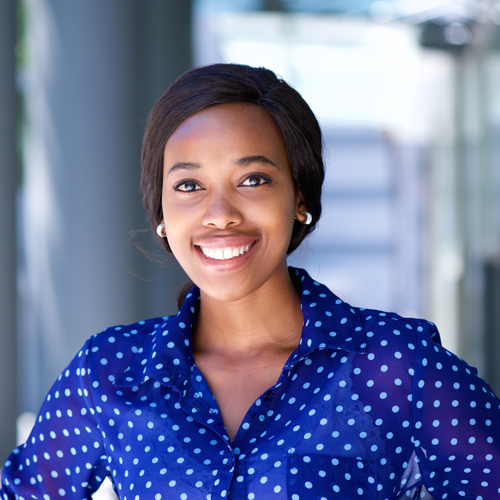 Smiling woman wearing a blue polka dot blouse standing in a bright indoor setting.