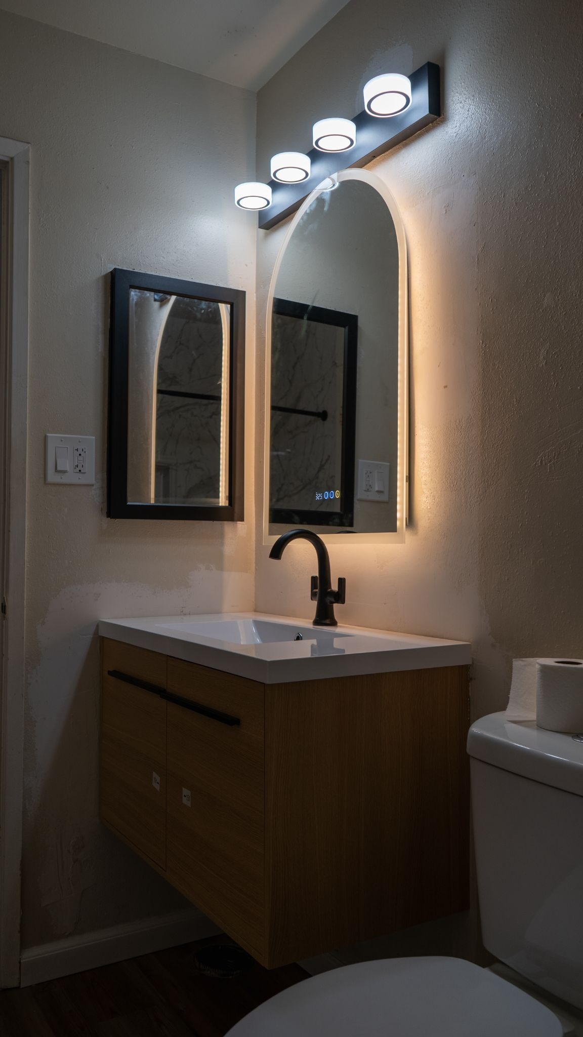 guest bathroom with layered lighting through lamps and LED lighting behind floating mirror