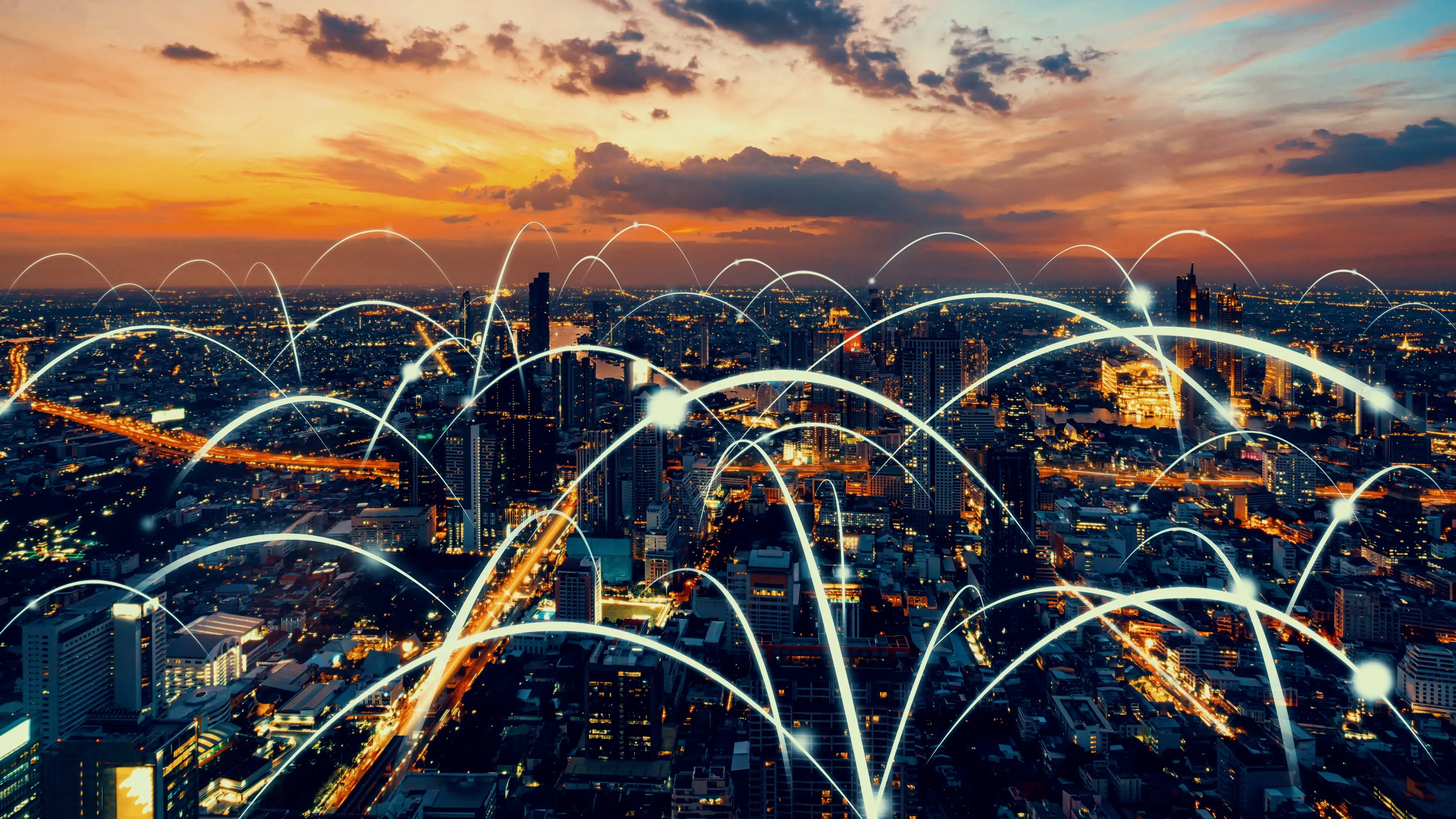 Stadt bei Sonnenuntergang mit leuchtenden, digital dargestellten Verbindungslinien über den Gebäuden.