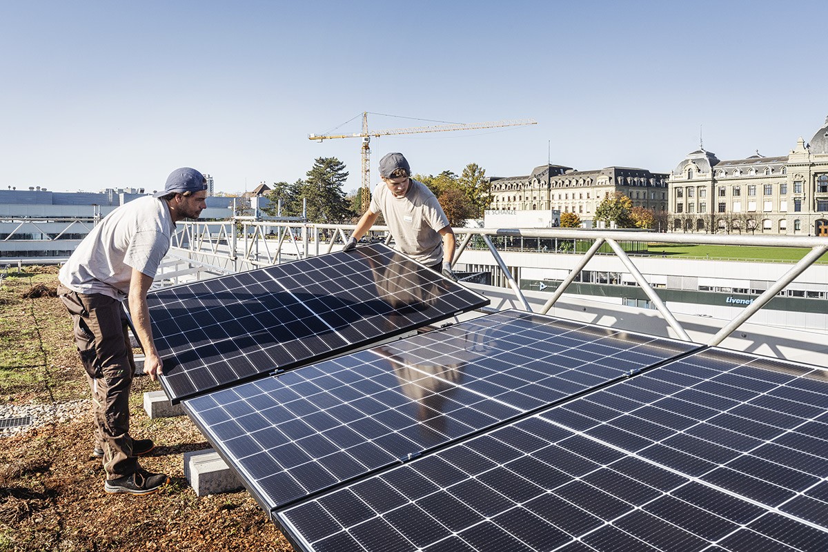 Vier Monteure installieren Solarpanels auf einem Flachdach mit Blick auf eine grüne Umgebung.