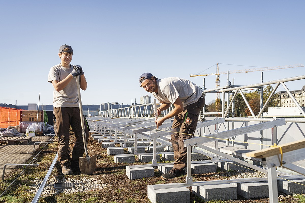 Drei Solarinstallateur:innen mit Helmen stehen selbstbewusst auf einem Dach. Text: 'Deine Zukunft ist Solar.