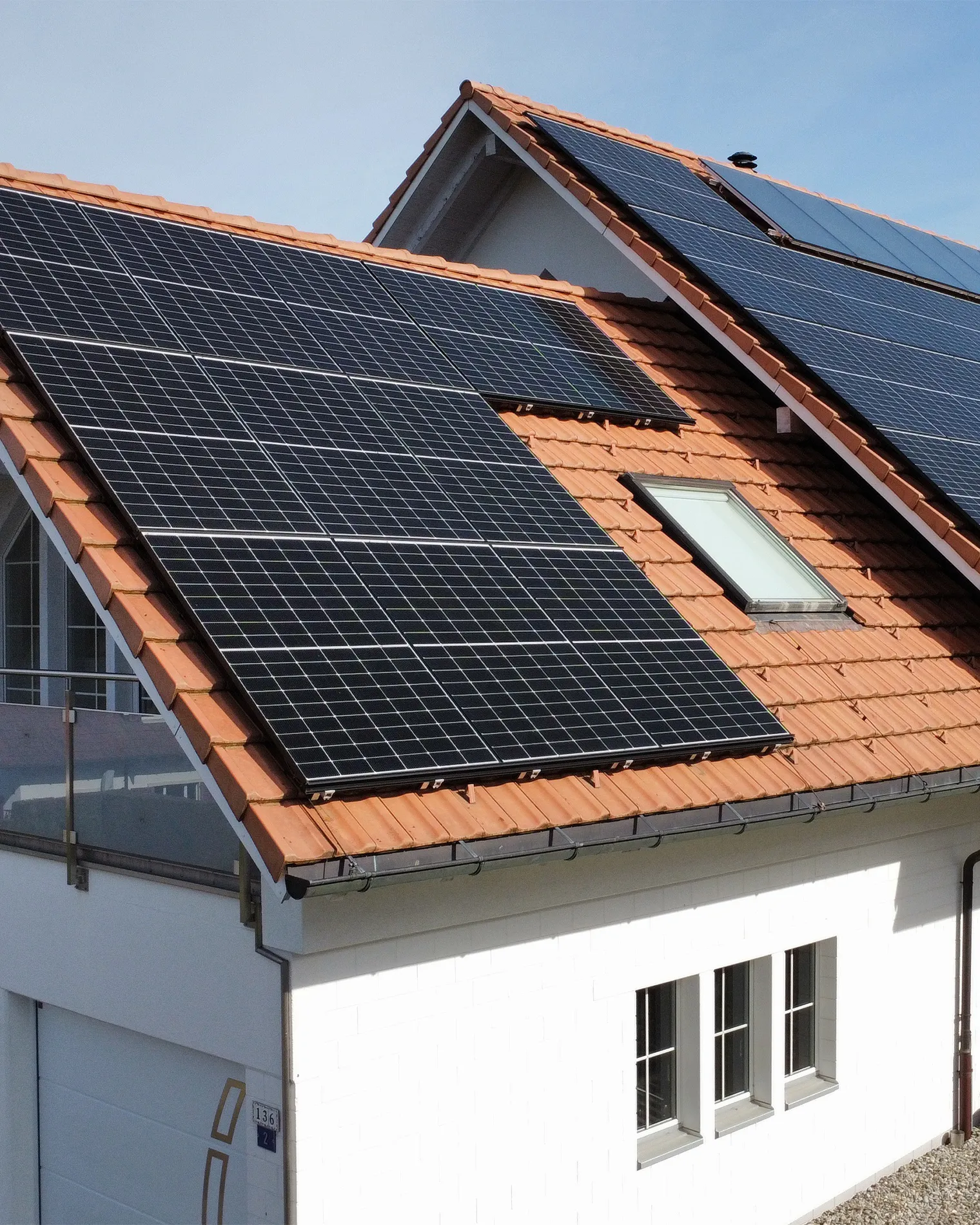 Draufsicht auf ein modernes Flachdachgebäude mit einer großflächigen Photovoltaikanlage. Die Solarpaneele sind in mehreren Reihen angeordnet, mit begrünten Flächen dazwischen.