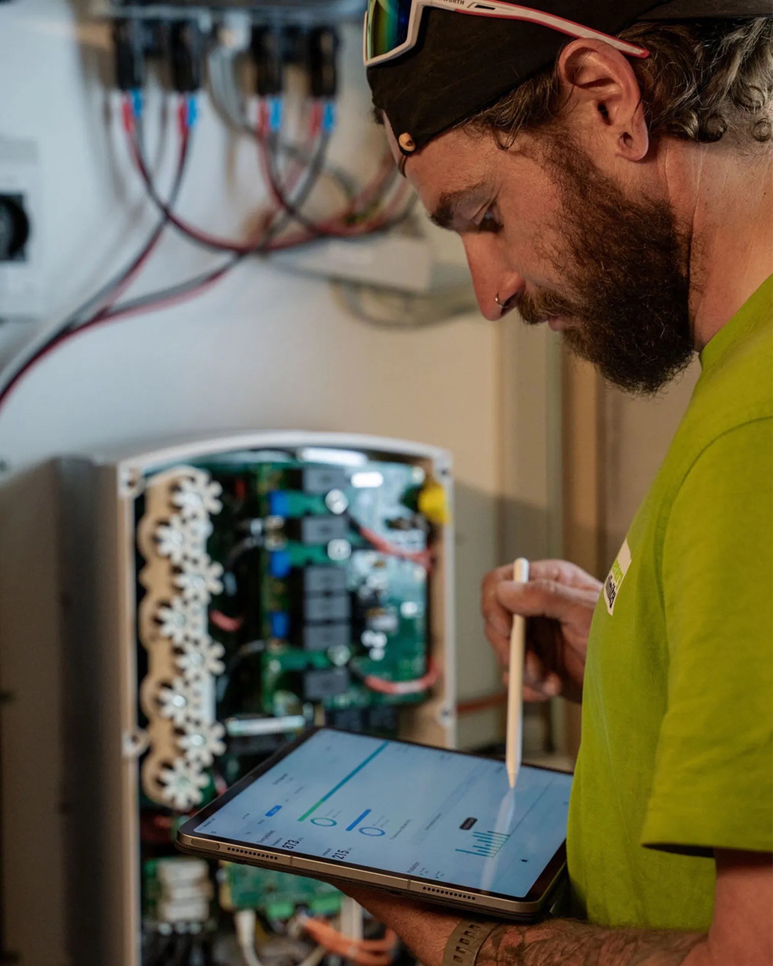 Ein Servicemitarbeiter von energy unlimited überprüft die Stromversorgung eines Einfamilienhauses auf dem Tablet. Hinter ihm der Stromspeicher, der auch am Abend den Strom für den Eigenverbrauch nutzbar macht.