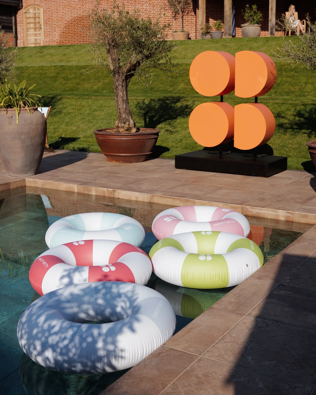 Colorful Sweaty Betty inflatable pool floats arranged by a swimming pool in a sunny outdoor setting.