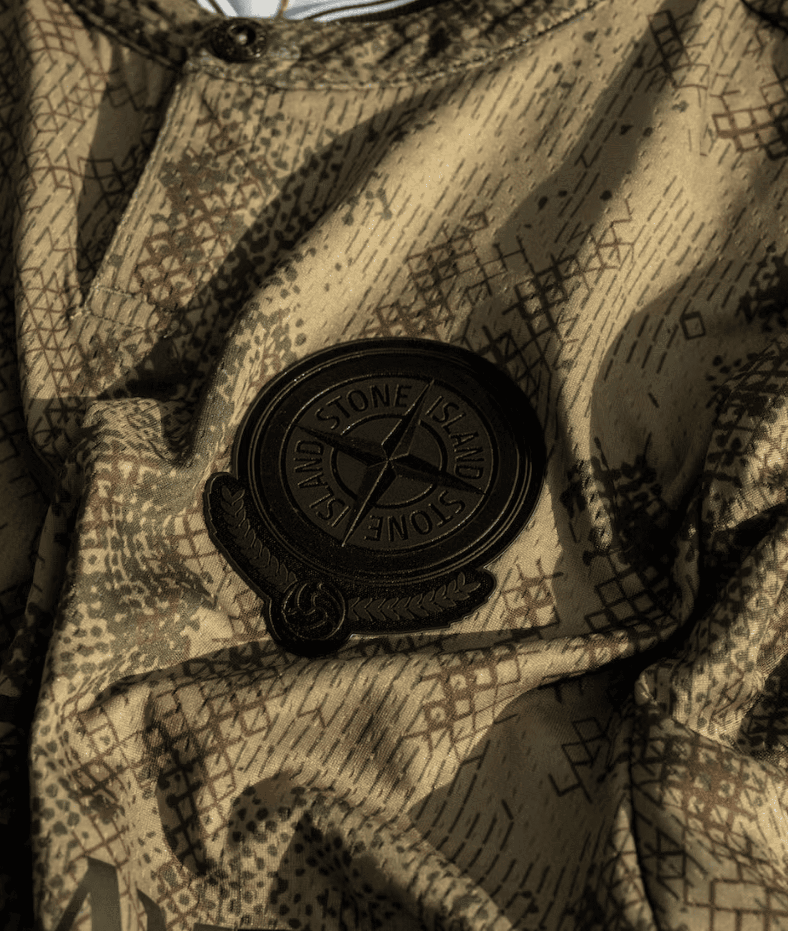 Close-up of the Stone Island compass logo on technical camouflage fabric from the New Balance collaboration kit.