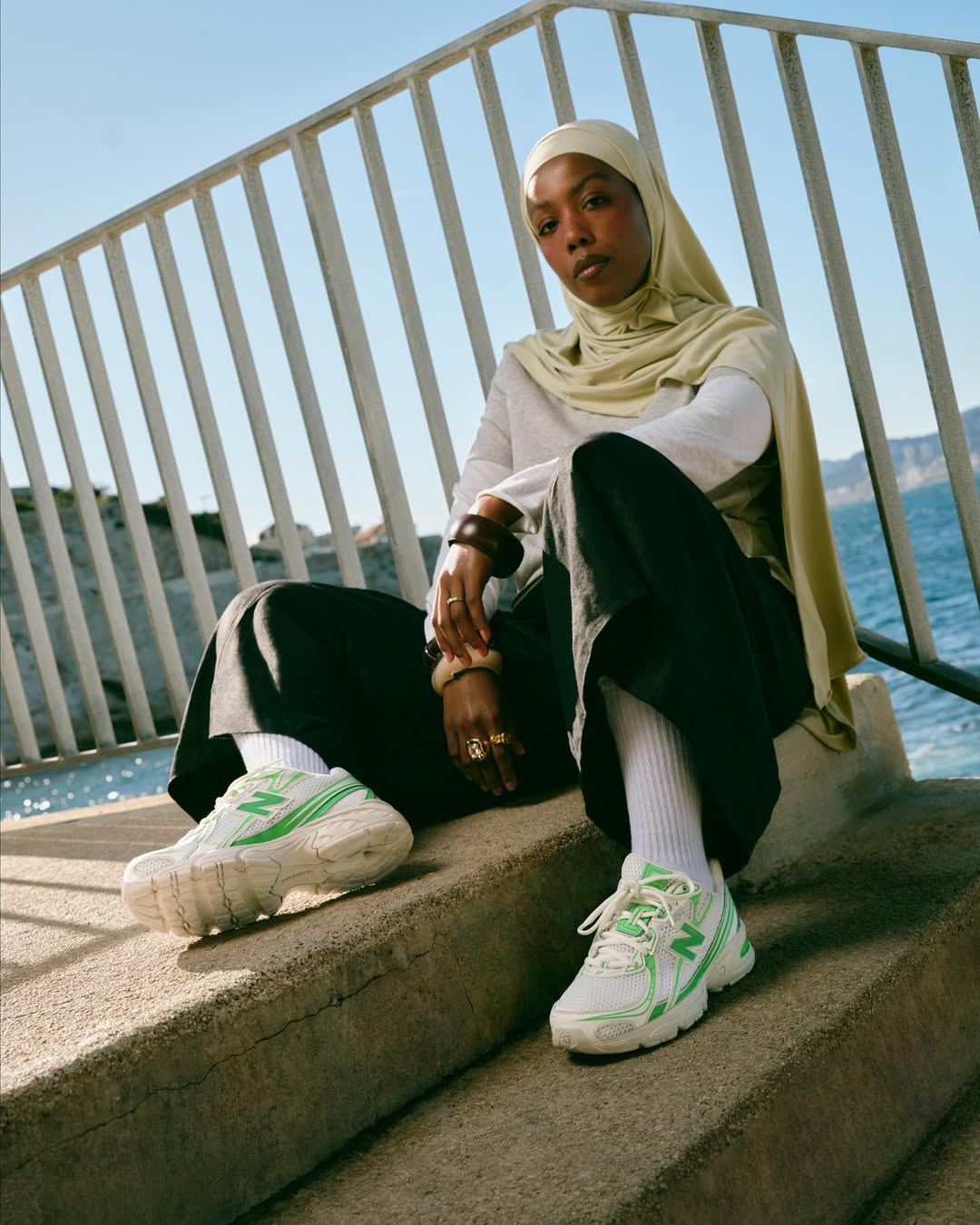 Close-up of model wearing New Balance x Foot Locker Club Ivy sneakers and layered streetwear by the seaside.