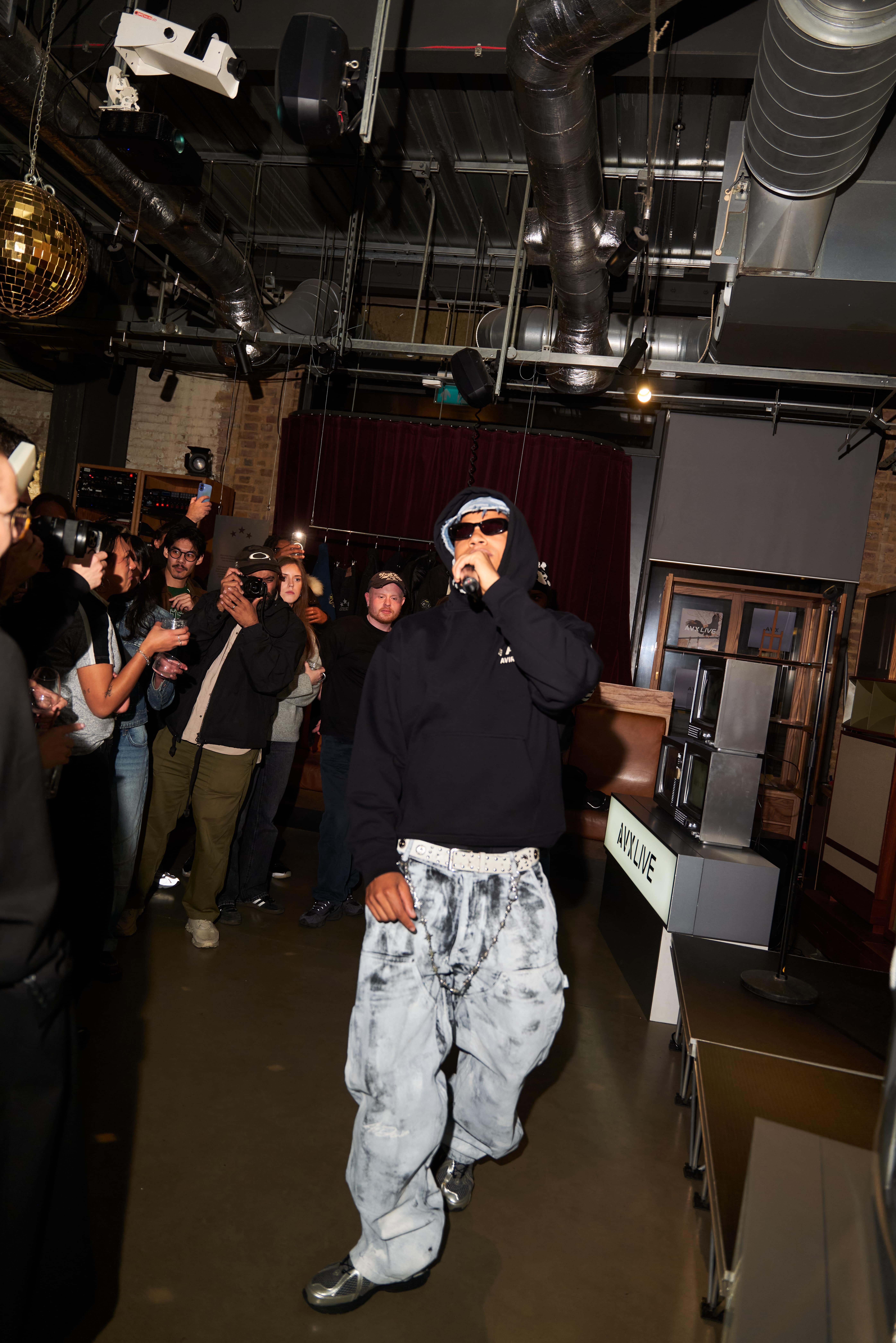 AntsLive performing in AVX hoodie and sunglasses on stage at AVX event.