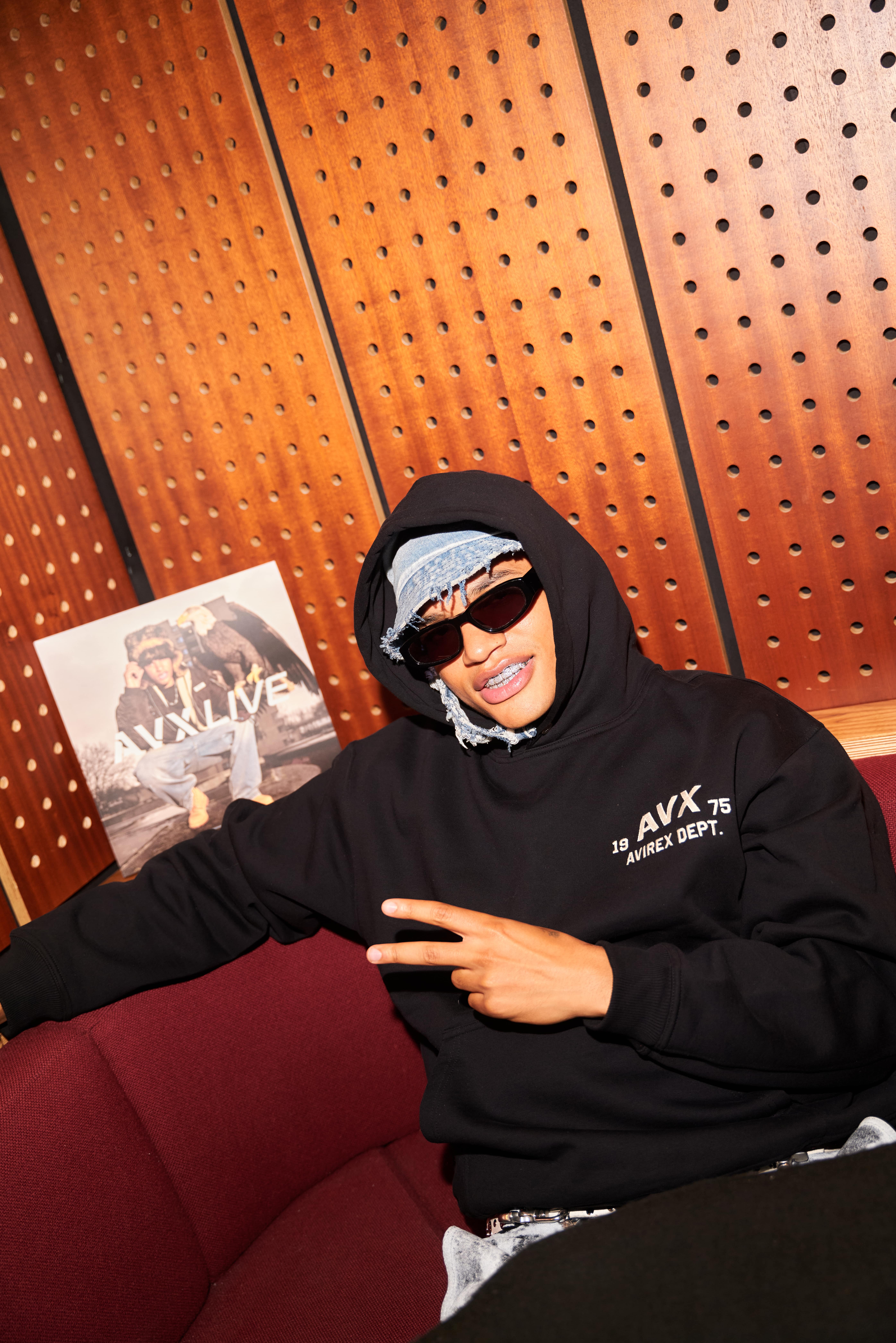 AntsLive wearing AVX hoodie and sunglasses holding AVX Live magazine during streetwear event photoshoot.