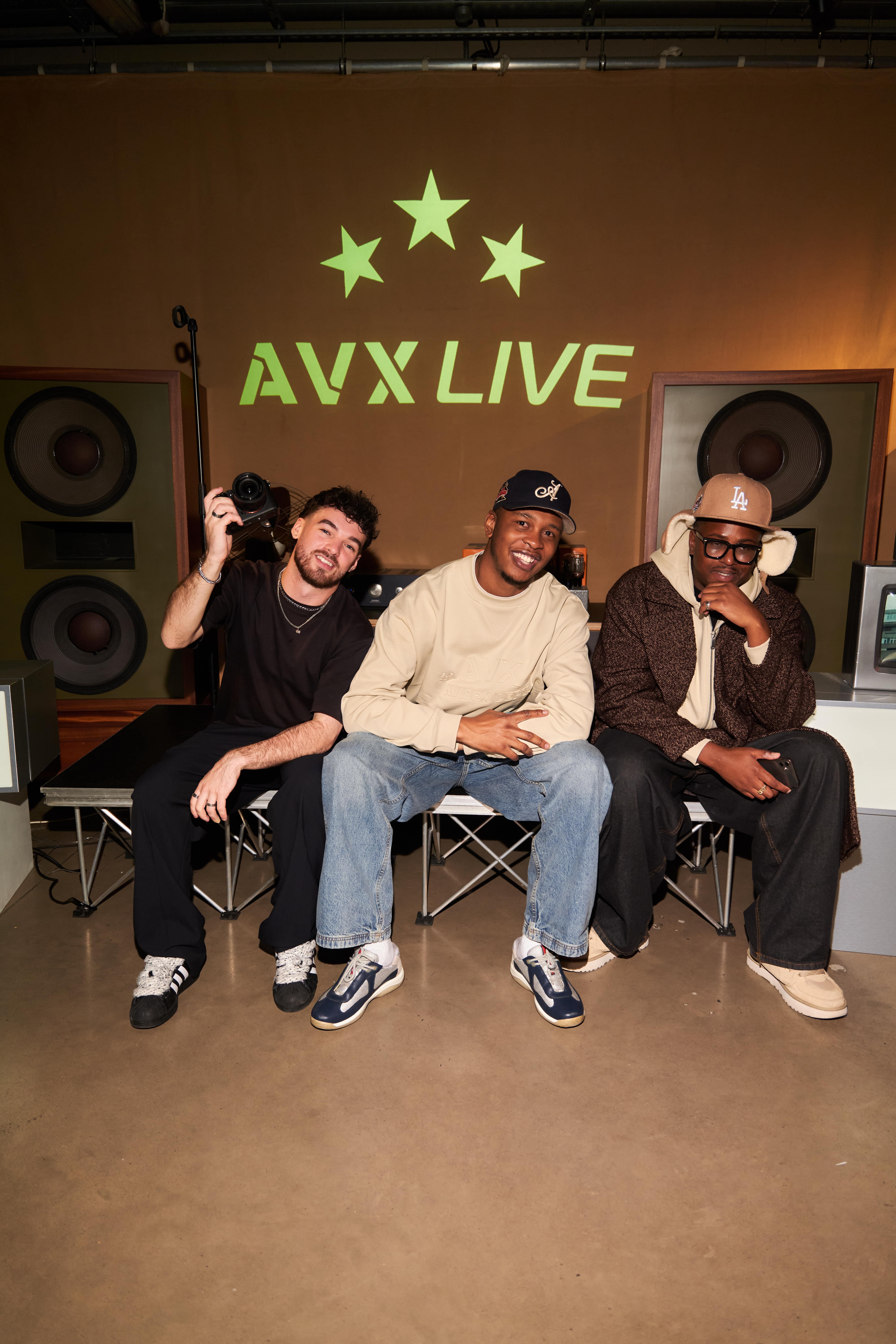 Guests posing together at the AVX Live event in casual streetwear surrounded by speakers and studio lighting.