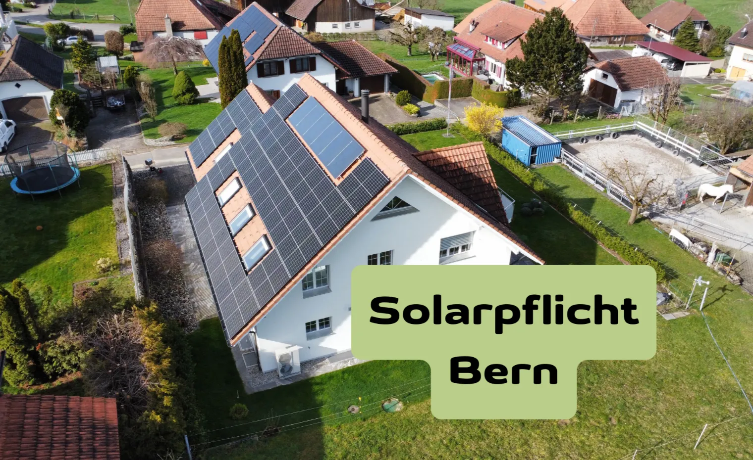 Luftaufnahme eines Einfamilienhauses mit grosser Photovoltaikanlage auf dem Dach, im Vordergrund der Schriftzug „Solarpflicht Schweiz“ – Symbolbild zur gesetzlichen Solarpflicht für Gebäude in der Schweiz.